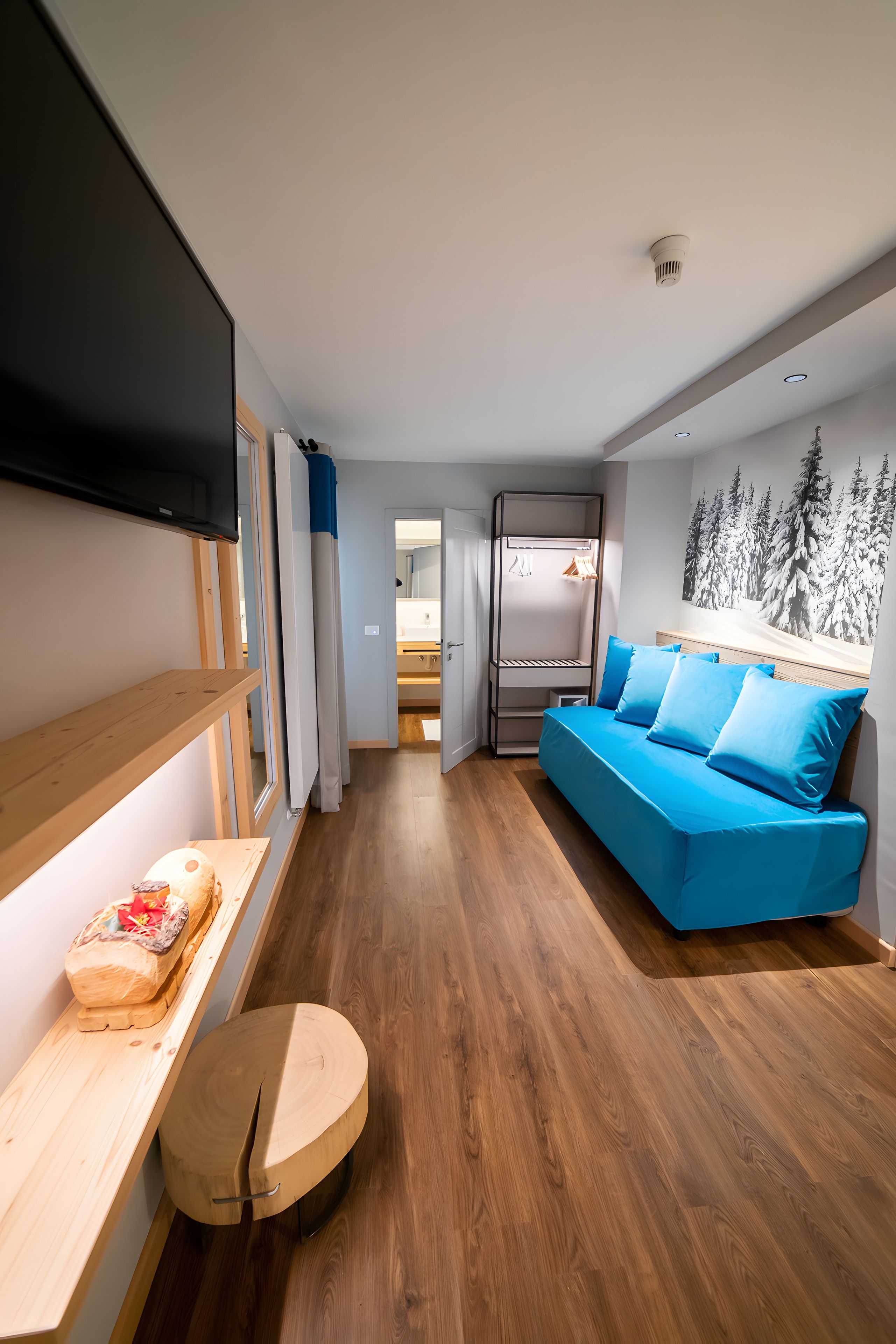 Een modern interieur met een houten vloer, een blauwe bank, een flatscreen televisie en een wandplank.