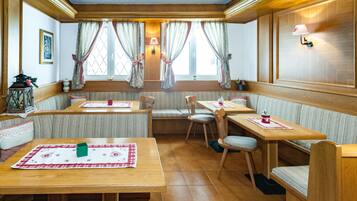 A cozy dining area with wooden tables and benches, a wall-mounted lamp, and a window with curtains.