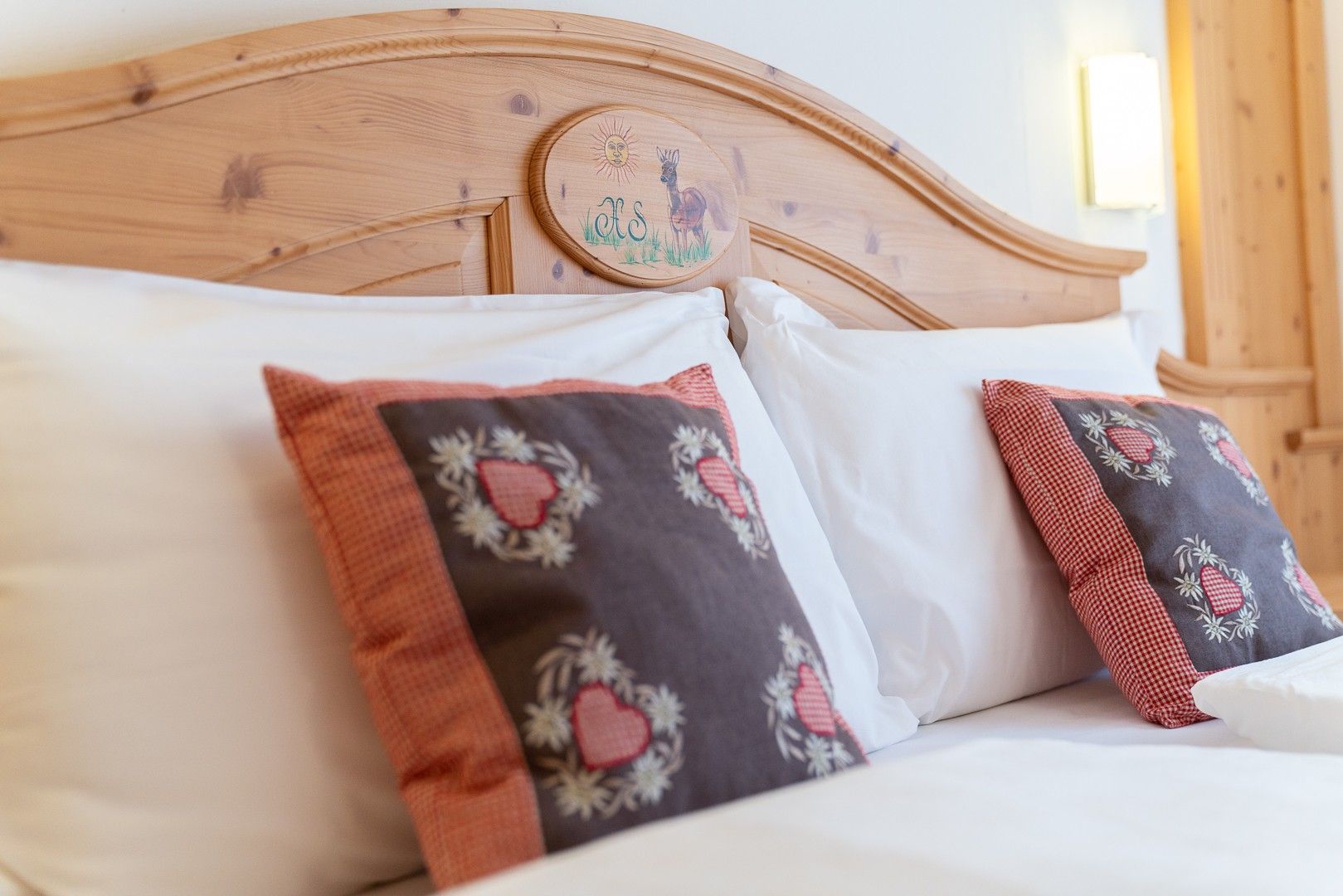 Un lit avec une tête de lit en bois, deux oreillers à motifs en forme de cœur et un couvre-lit blanc.