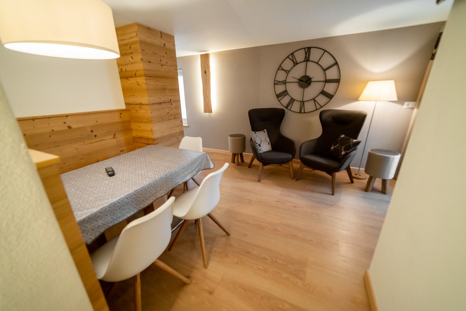 Ein modernes Interieur mit einer Wand in Holzoptik, einer großen Wanduhr und einem Essbereich mit Stühlen und Tisch.