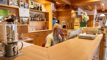 A wooden interior with a bar area, shelves with bottles, and a person at a counter.