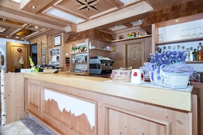 A wooden bar area with shelves of bottles, a coffee machine, and a decorative vase with flowers. - 'Betulla' Room with Mountain View, Shared Terrace, and Wi-Fi (San Sebastiano)