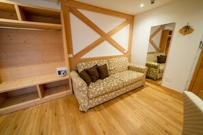 A room with a wooden floor, a patterned sofa, and a wooden shelf unit. - Sciatore Room with Mountain View, Shared Terrace and Wi-Fi (San Sebastiano)