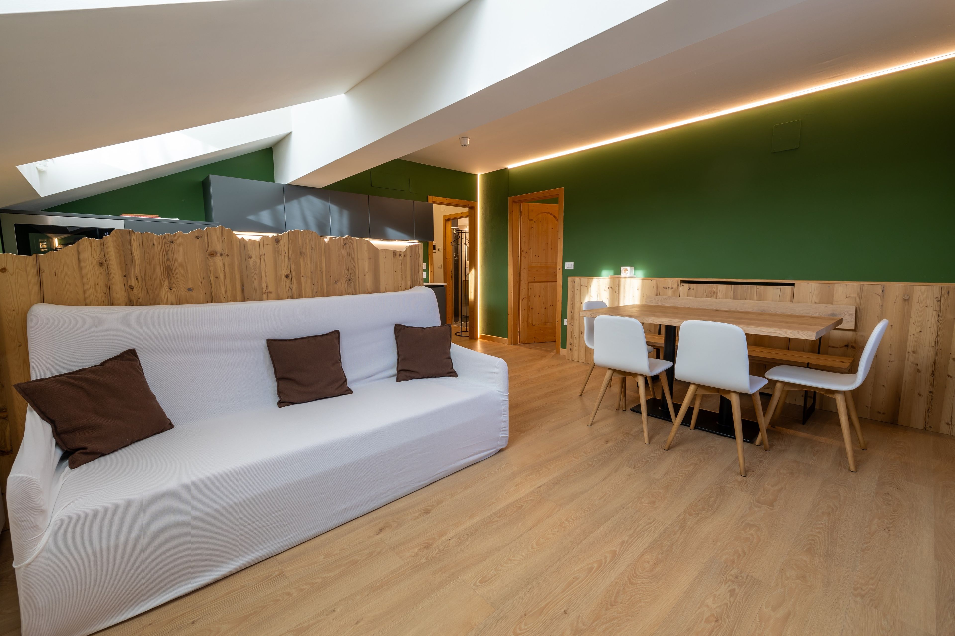 Ein modernes Interieur mit einem weißen Sofa, Holzelementen, einem Essbereich und einer grünen Wand.
