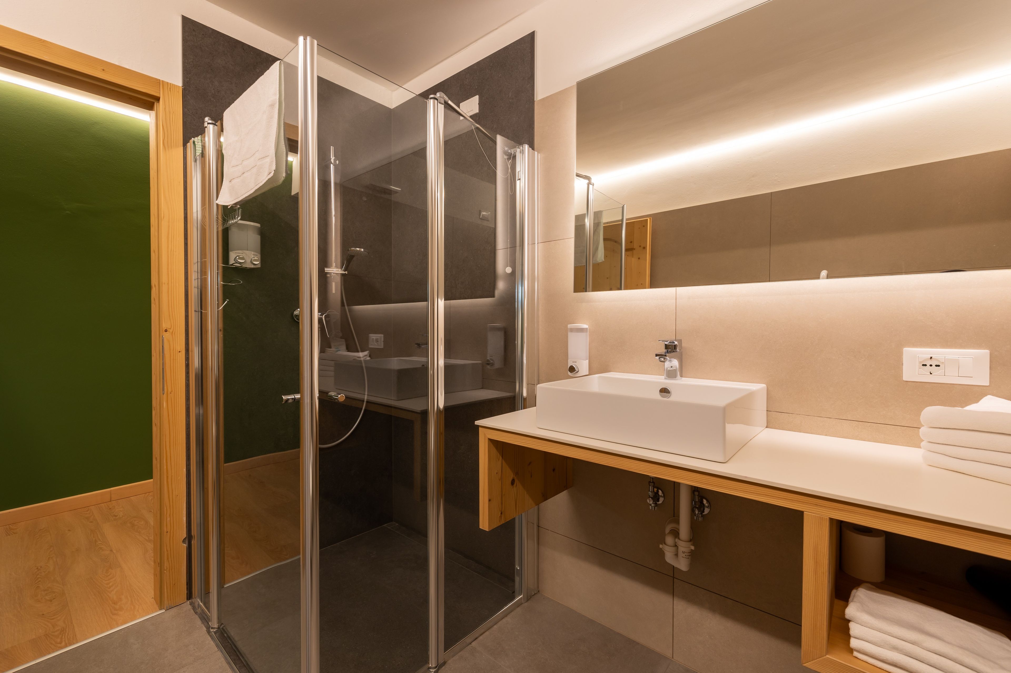 Une salle de bain moderne avec une douche à parois de verre, un lavabo blanc et un miroir au-dessus du meuble-lavabo.