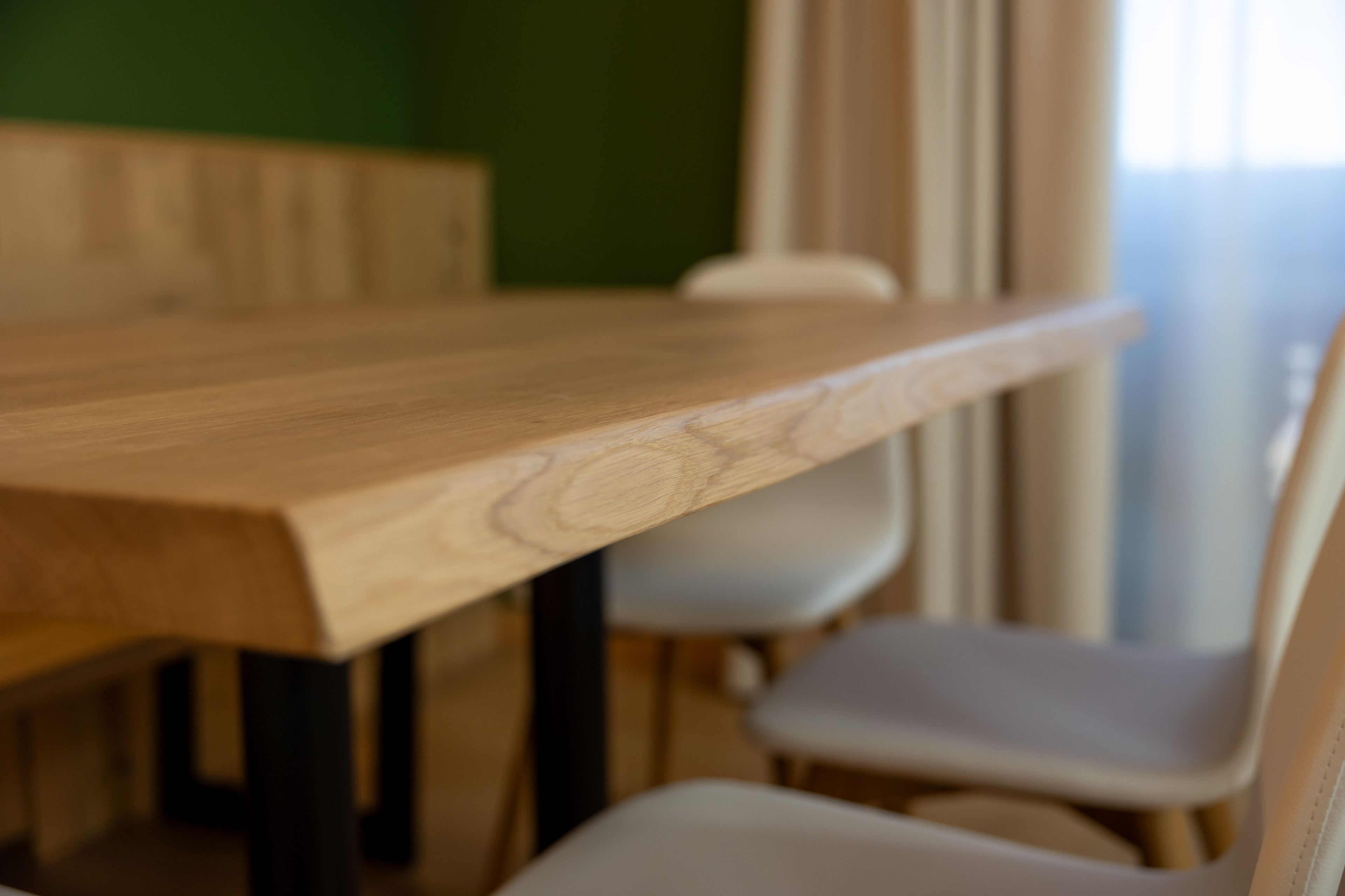 A wooden dining table with chairs, a green wall, and a window with curtains.
