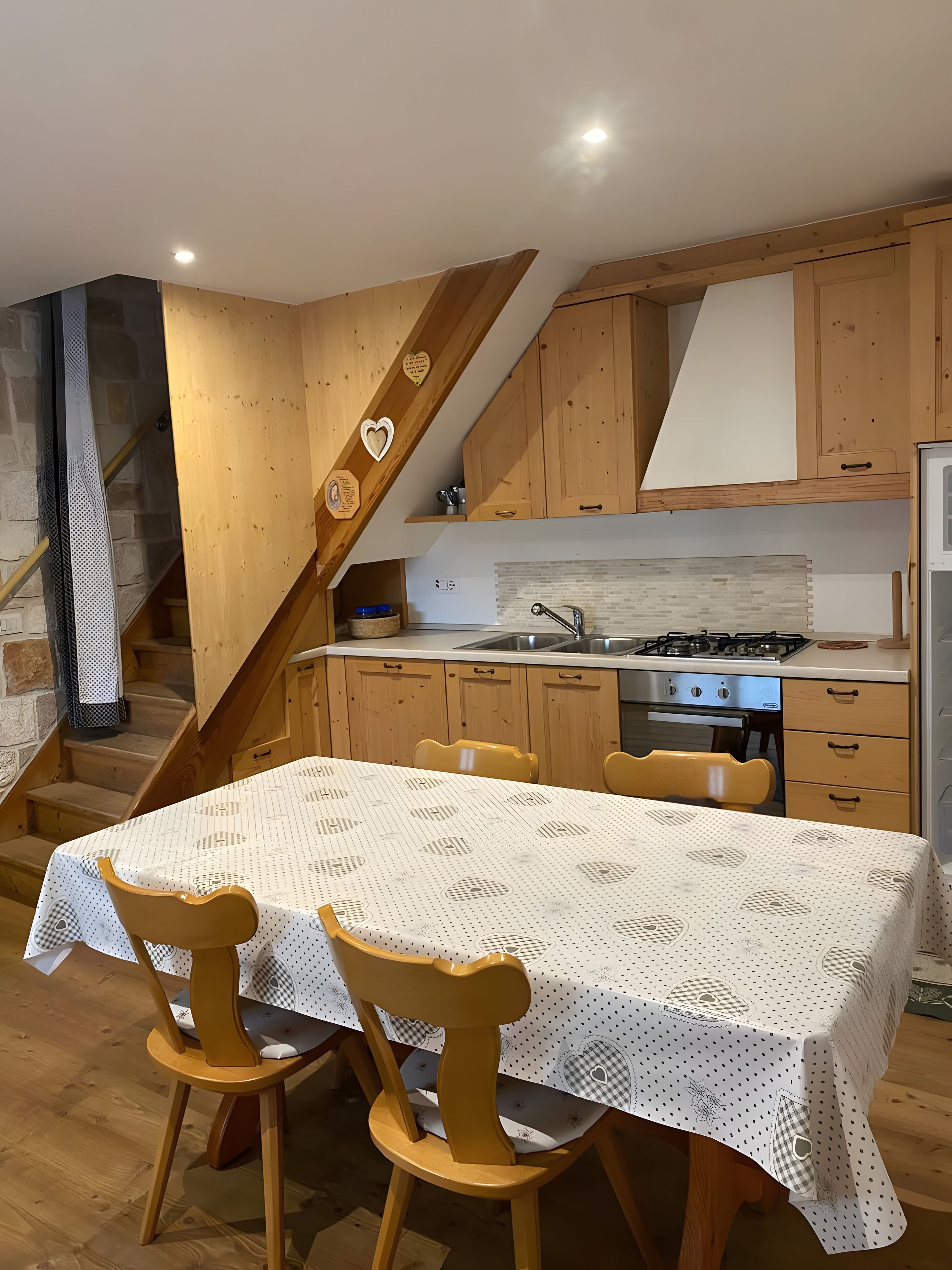 Une cuisine avec des meubles en bois, une table à manger avec des chaises et un escalier orné d’un motif en forme de cœur.