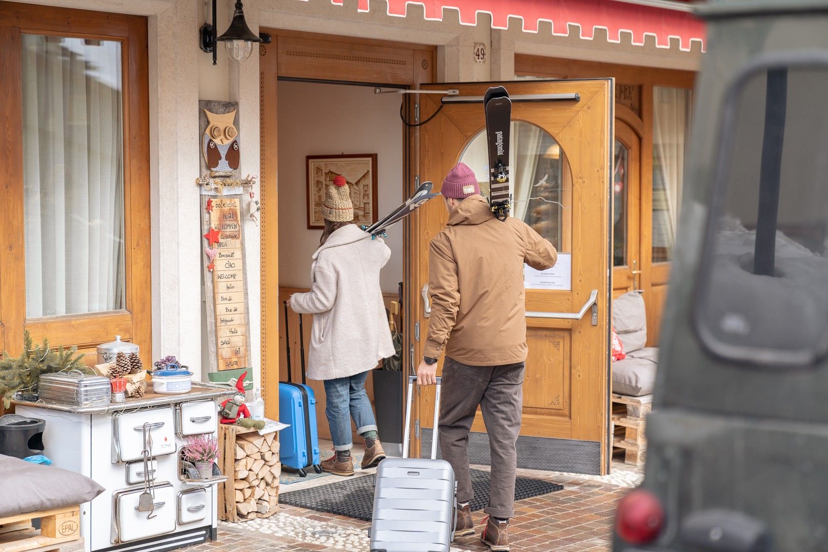 Een houten deur met een bordje, een persoon met een ski stok en een blauwe koffer op de grond.