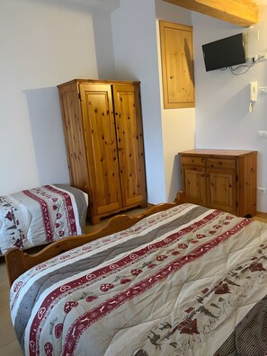 Quarto com duas camas de madeira, um guarda-roupa, uma televisão na parede e uma mesa de cabeceira.