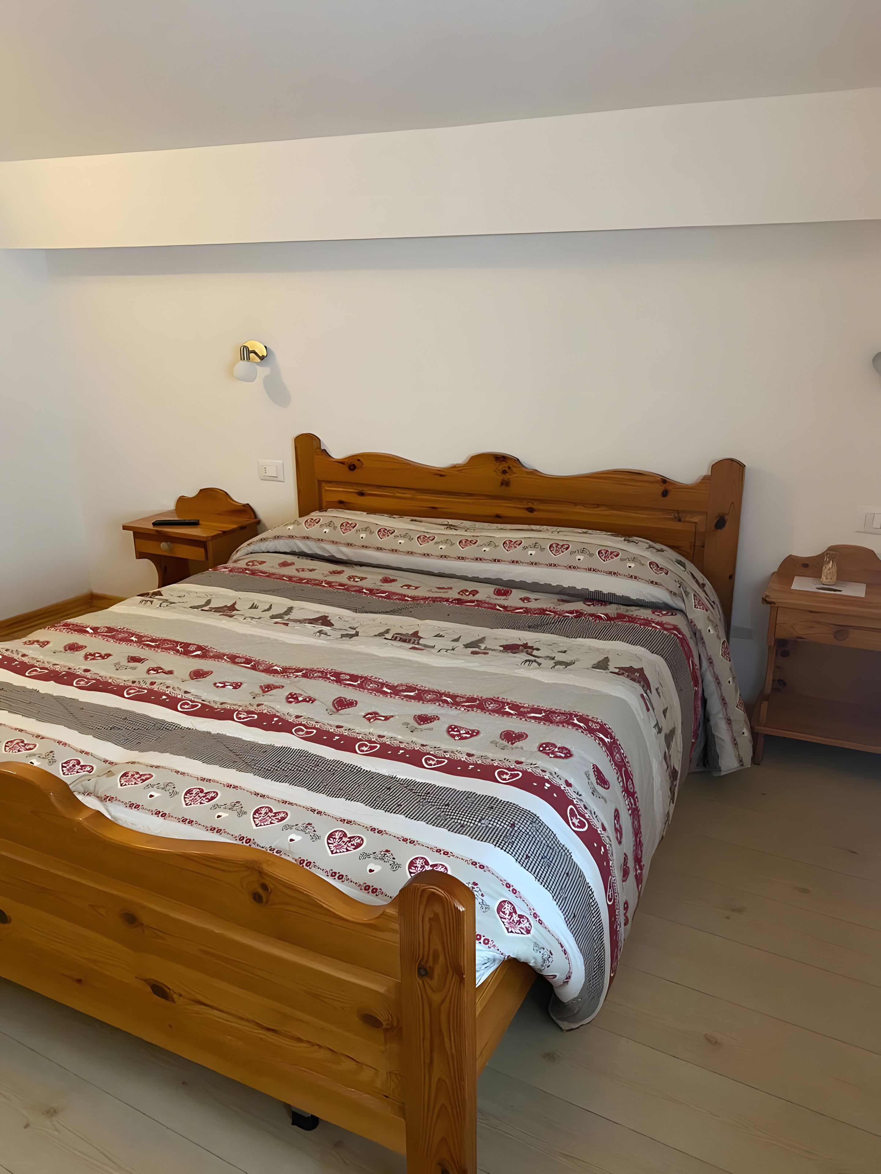 Un lit en bois avec une couvre-lit à motifs, une table de chevet et une petite table de nuit.