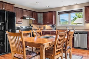 A kitchen with wooden cabinets, a dining table with chairs, and a view of the outdoors through a window.