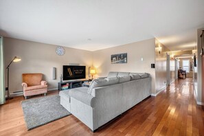 A modern living room with a grey sofa, a pink armchair, a flat-screen TV, and a wooden floor.