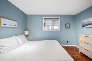 A bedroom with a bed, a nightstand, a lamp, a dresser, a window, and wall art.