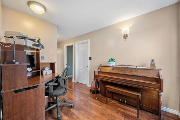 A home office with a desk, chair, and a piano.
