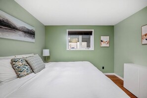 A bedroom with a bed, pillows, a window, and a radiator.
