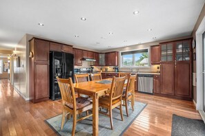 A modern kitchen with wooden cabinets, a dining table with chairs, and a large window.