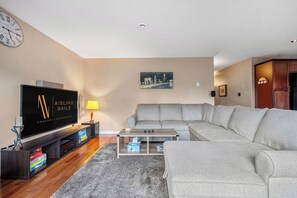 A living room with a sectional sofa, a flat-screen TV, a coffee table, and a lamp.