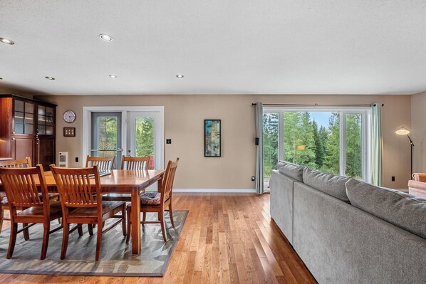 A modern interior with a dining area, a sofa, and a view of the outdoors.