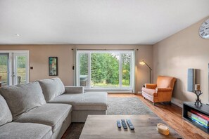 A living room with a grey sofa, a wooden coffee table, and a chair. There are three remote controls on the table.