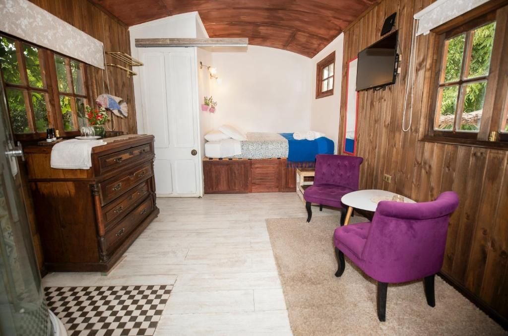 A room with a wooden ceiling, a bed with a blue cover, a dresser, a purple chair, and a small table.