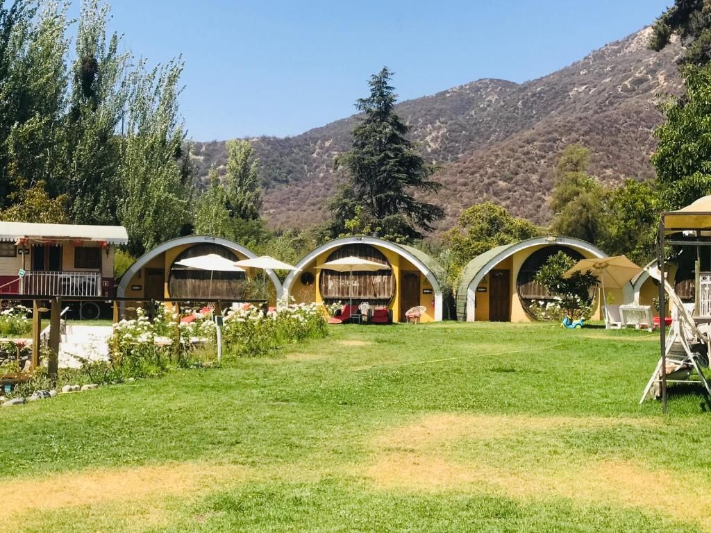 A series of dome-shaped buildings with outdoor seating areas, surrounded by a grassy field and trees, with a mountainous backdrop.