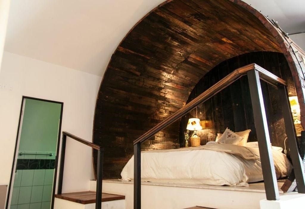 A bedroom with a curved wooden ceiling, a bed with white linens, and a green door.