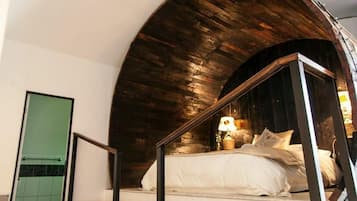 A bedroom with a curved wooden ceiling, a bed with white linens, and a green door.