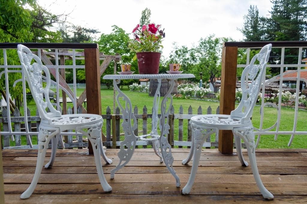 Two white metal chairs and a small table with a potted plant on a wooden deck.