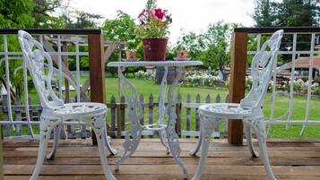 Duas cadeiras de metal branco e uma pequena mesa com um vaso de planta em um deck de madeira.