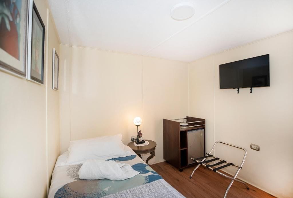 Una camera d'albergo con un letto, una scrivania, una sedia, una televisione e un tavolino con una lampada.