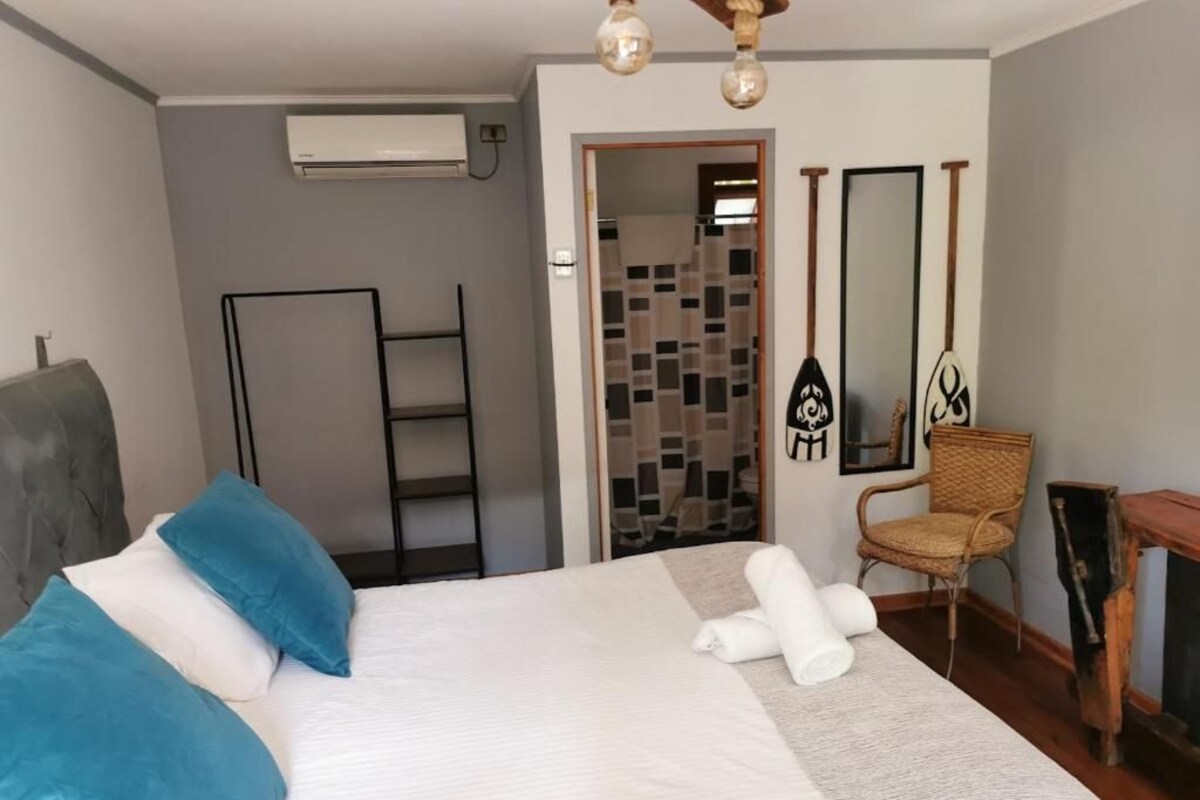 A hotel room with a bed, a chair, a small table, a mirror, and a door leading to a bathroom.