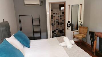 A hotel room with a bed, a chair, a small table, a mirror, and a door leading to a bathroom.