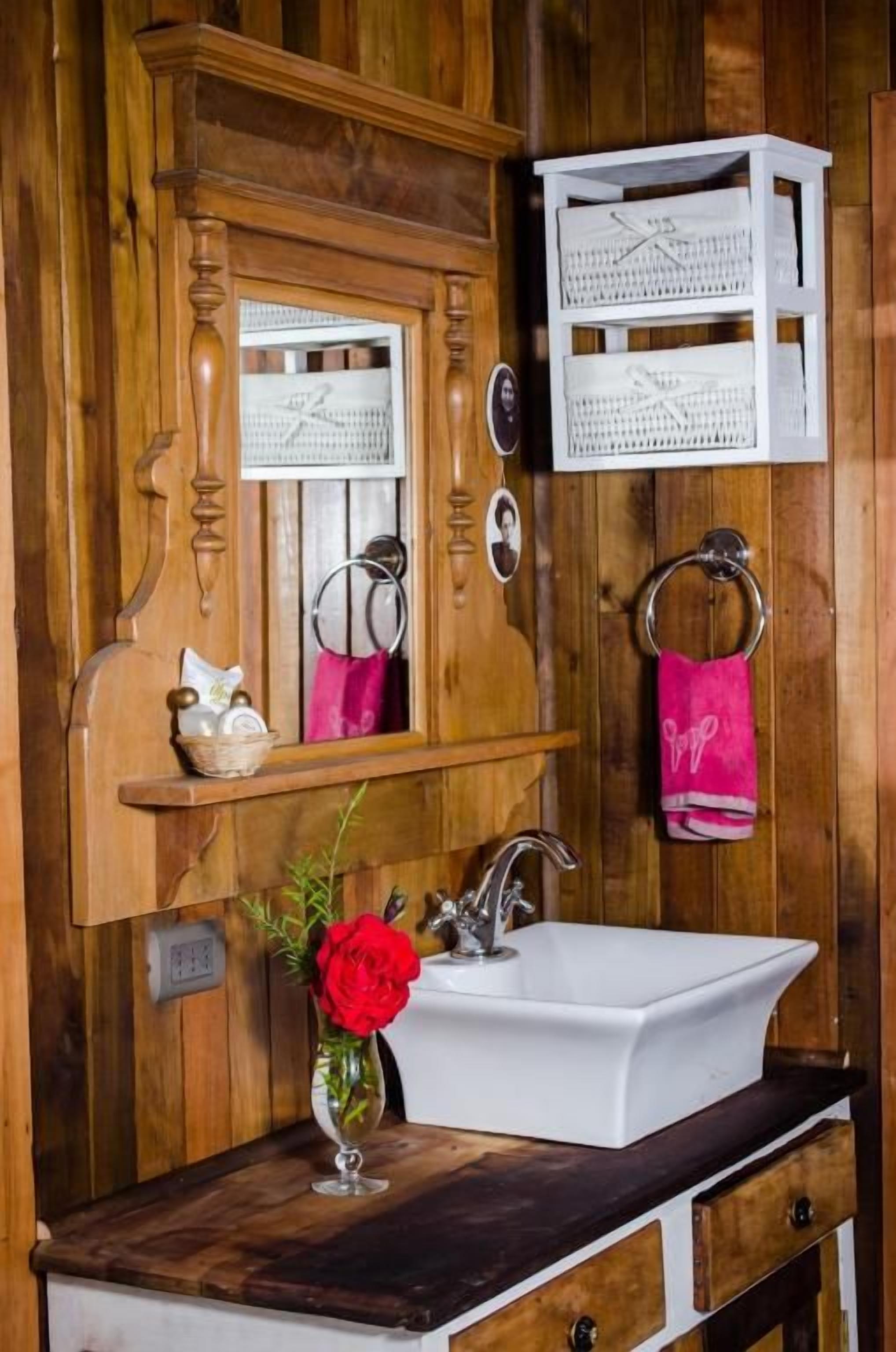 A wooden bathroom with a white sink, a mirror, and a shelf with a pink towel.