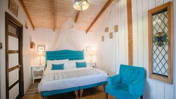 A bedroom with a bed, bedside lamps, a chair, a window with a decorative glass, and wooden beams on the ceiling.
