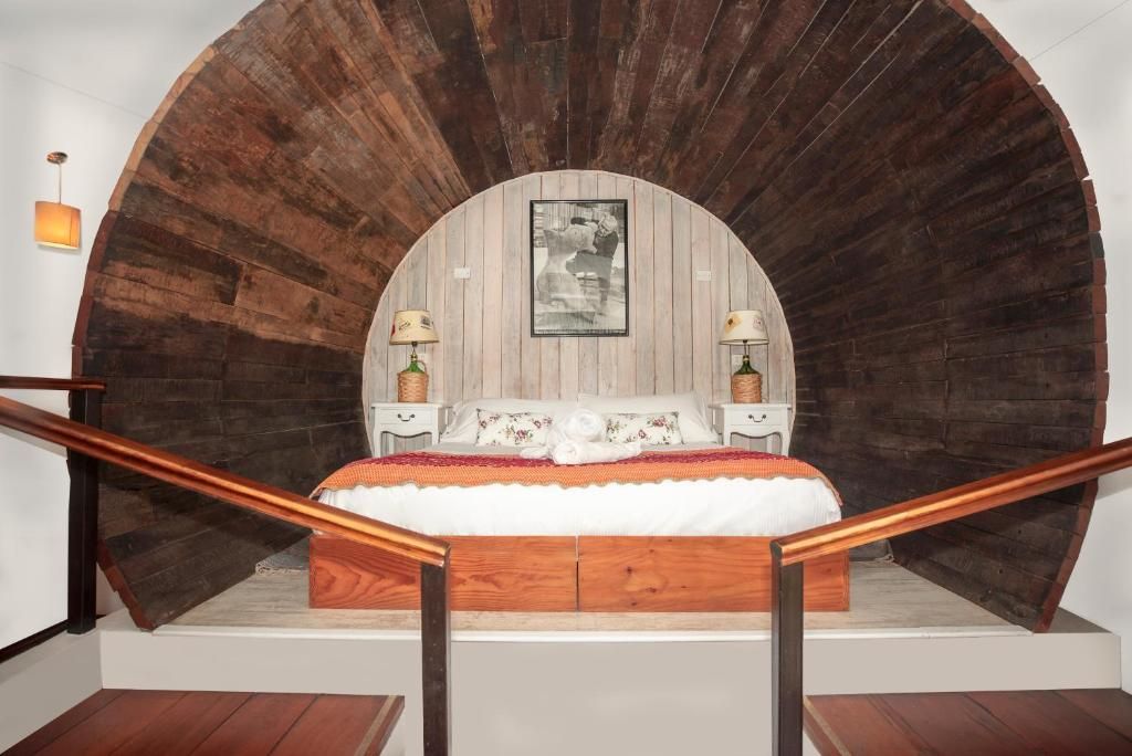 Quarto com teto em arco de madeira, cama com roupa de cama branca, duas mesas de cabeceira com abajures e um quadro na parede.