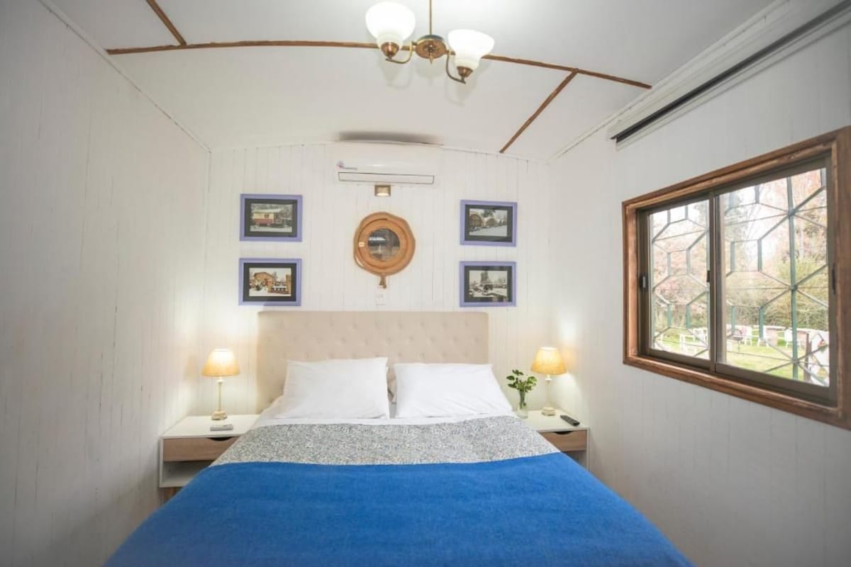 Une chambre à coucher avec un lit, deux tables de chevet, une horloge murale et une fenêtre donnant sur un paysage agréable.