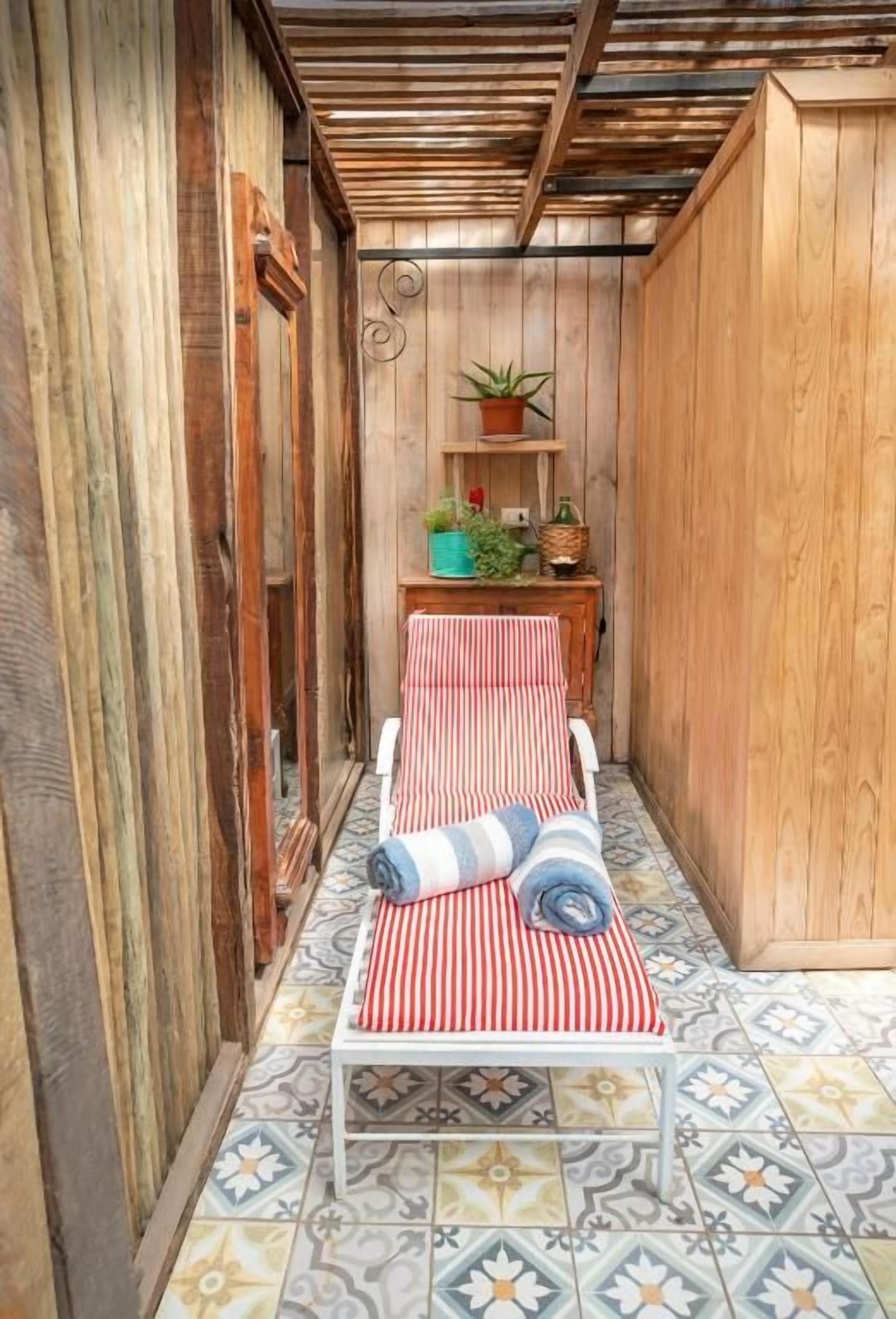 A narrow corridor with a bench, a shelf with plants, and a patterned floor.