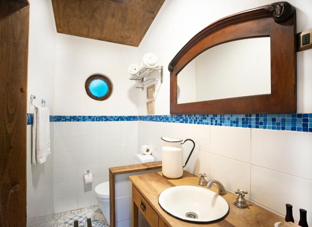 Un baño con lavamanos blanco, tocador de madera, espejo redondo y zona de ducha con azulejos azules.
