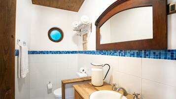 Un baño con lavamanos blanco, tocador de madera, espejo redondo y zona de ducha con azulejos azules.