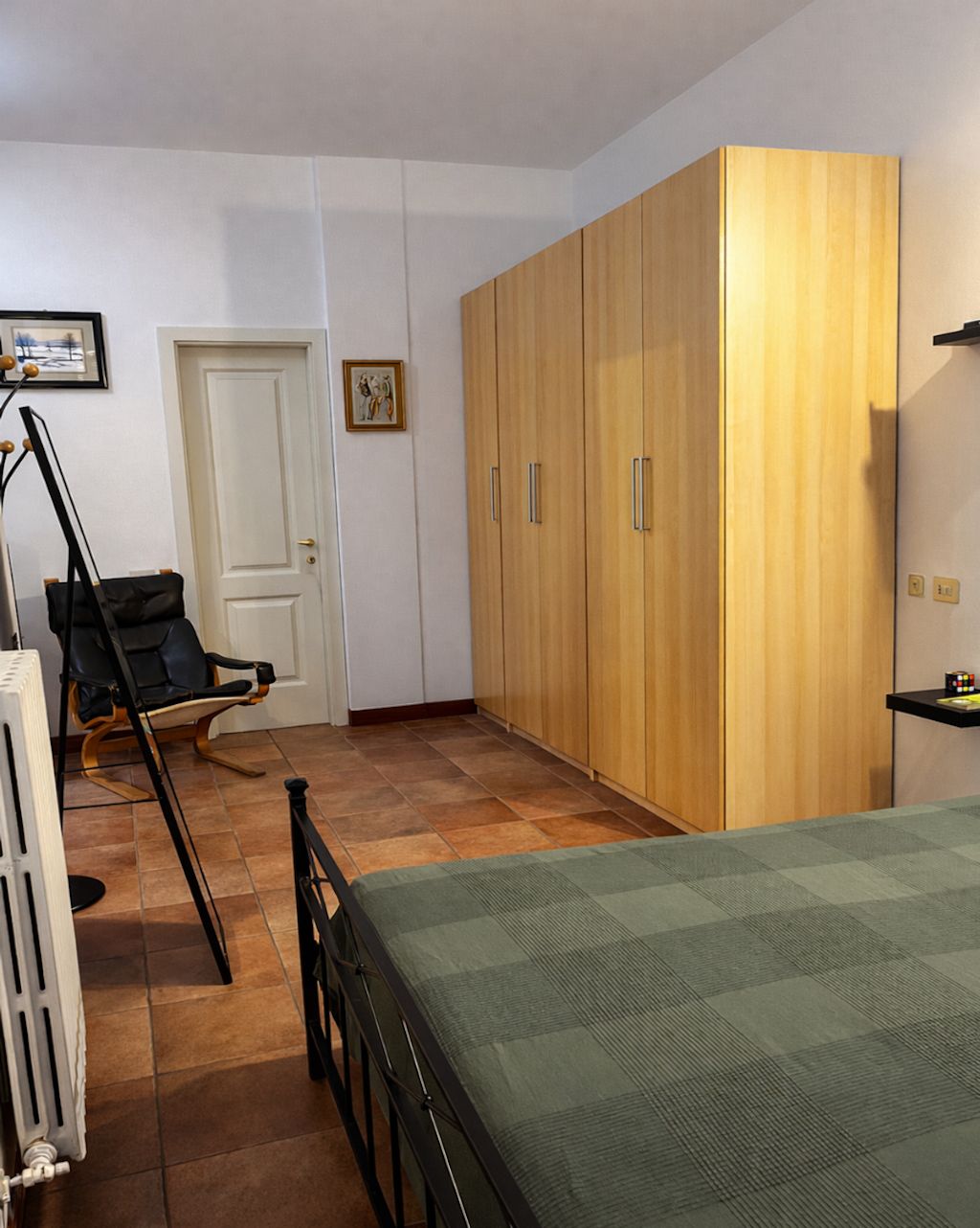Ein Schlafzimmer mit Bett, einem Holzschrank, einem Sessel und einem Heizkörper.