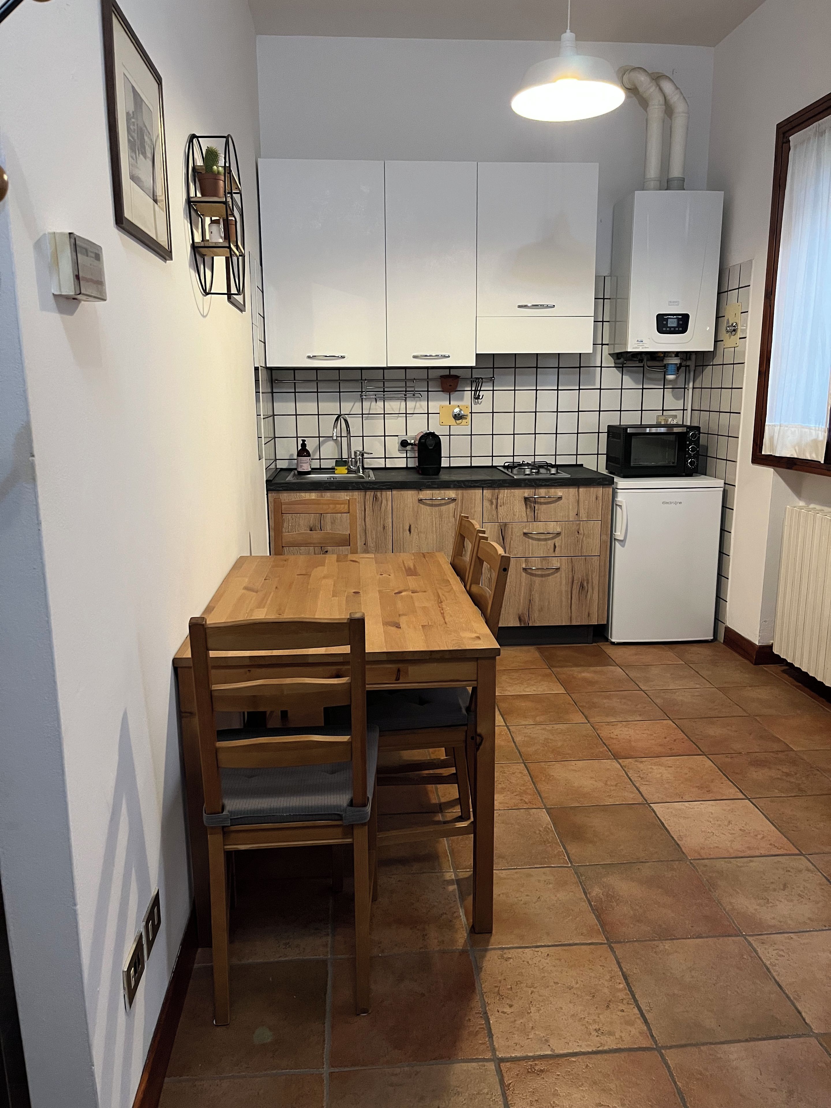 Ett kompakt kök med vita skåp, ett matbord i trä och en inbyggd mikrovågsugn.