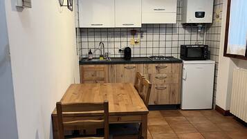 Ett kompakt kök med vita skåp, ett matbord i trä och en inbyggd mikrovågsugn.