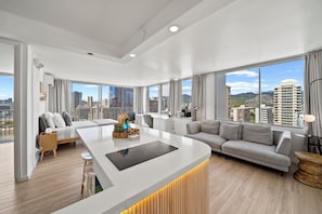 A modern living room with a central island, a sofa, and a dining area. - 0.1 Mile to Beach 23FL 1BR 2BED Ocean/Mountain Views RF TOP Pool Central Waikiki (Honolulu)