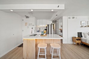 Eine moderne Küche mit einer zentralen Kochinsel, zwei Barhocker und einem Essbereich mit einer Couch und einem Nachttisch.