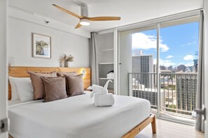 A modern hotel room with a large bed, a ceiling fan, a city view, and a balcony. - 0.1 Mile to Beach 23FL 1BR 2BED Ocean/Mountain Views RF TOP Pool Central Waikiki (Honolulu)