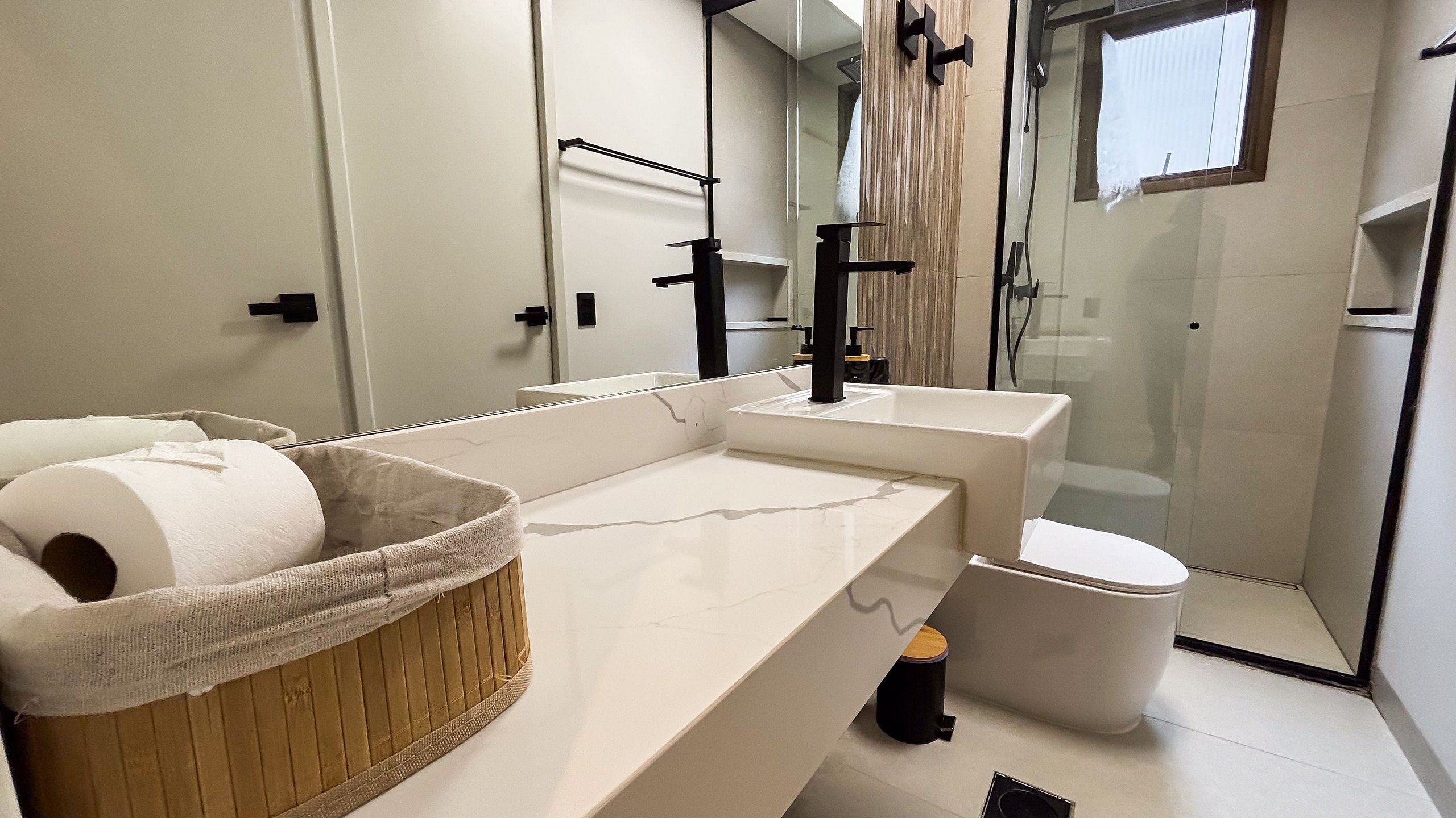 Un baño moderno con una encimera blanca, un grifo negro, un inodoro y una cabina de ducha de vidrio.