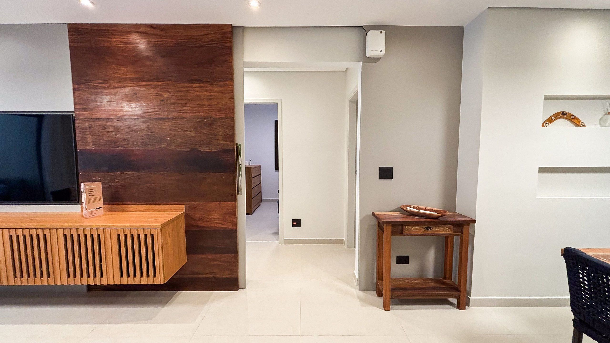 A modern living room with a wooden console table, a small wooden side table, and a flat-screen TV mounted on the wall.