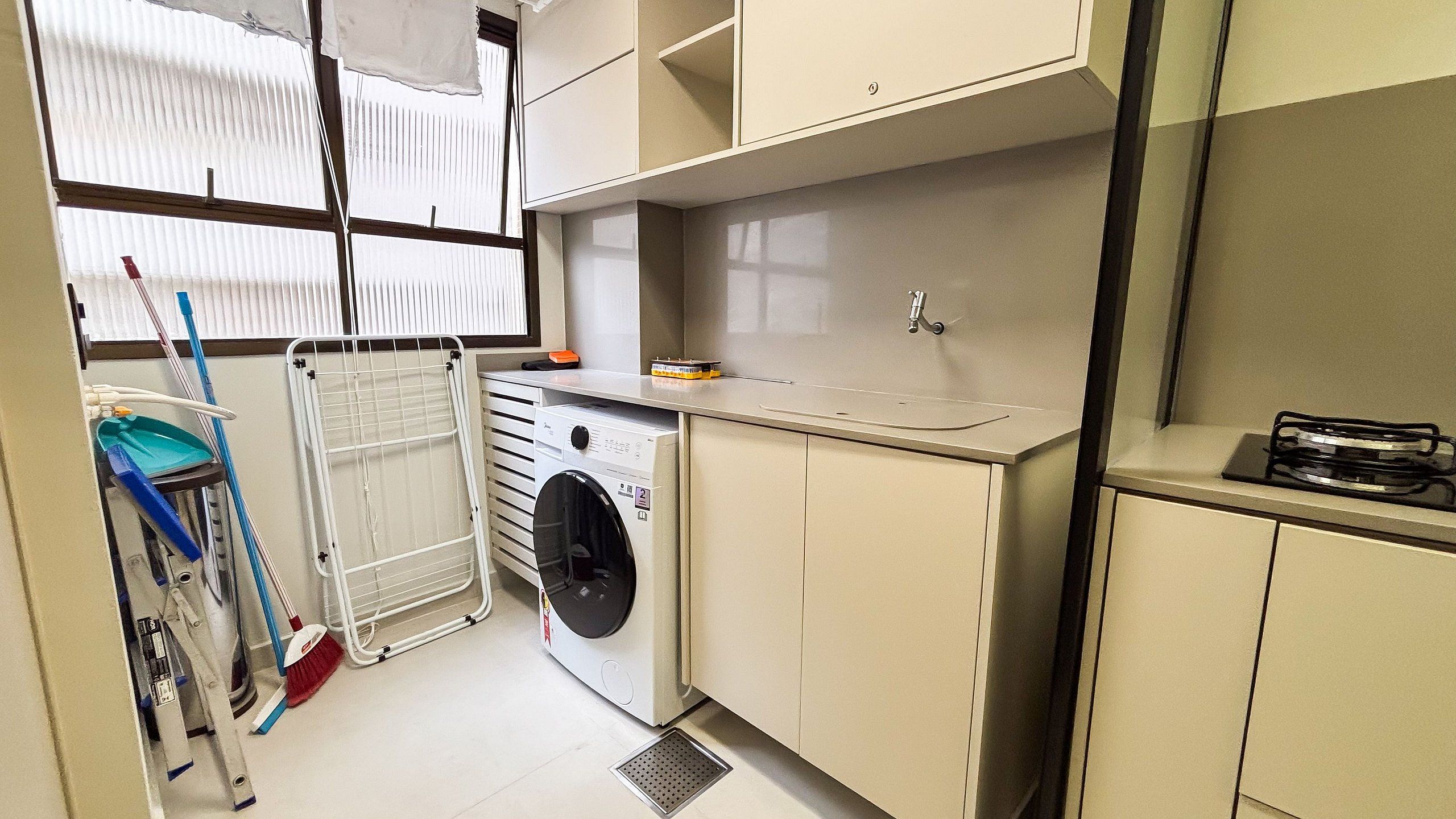 A compact laundry room with a washing machine, drying rack, and a small countertop with a sink.