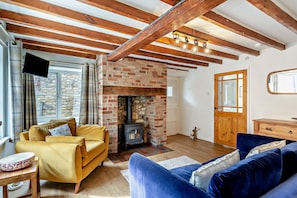 A cozy living room with a brick fireplace, wooden beams, a sofa, and a television. - Host Stay - Hatton Rose Cottage (York)