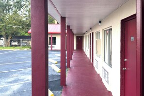 A motel corridor with red pillars, a covered walkway, and a parking lot.